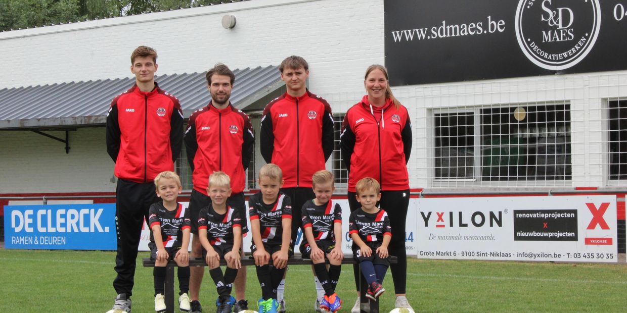 Een jeugdvoetbalteam met coaches poseert op het veld.