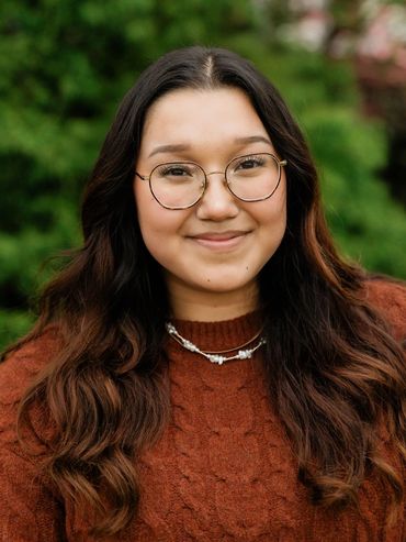 Young woman with glasses smiling outdoors.