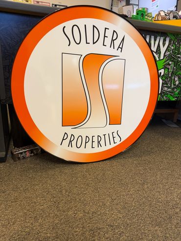 Round sign for Soldera Properties with orange and white design.