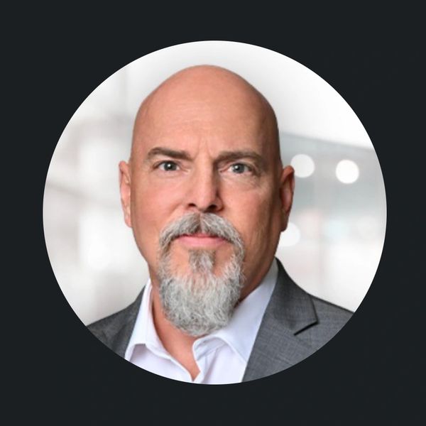 Bald man with gray beard in suit jacket.