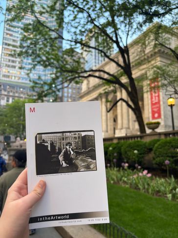 Person holding a book in a city park.