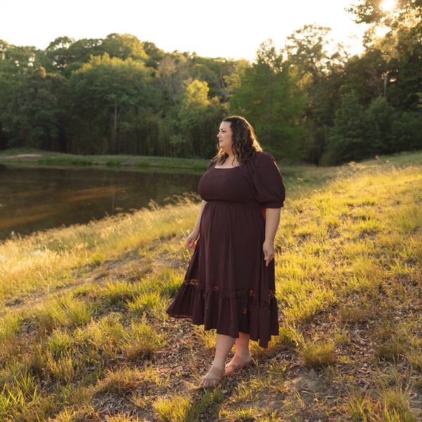 Woman in purple dress standing by a lake at sunset.