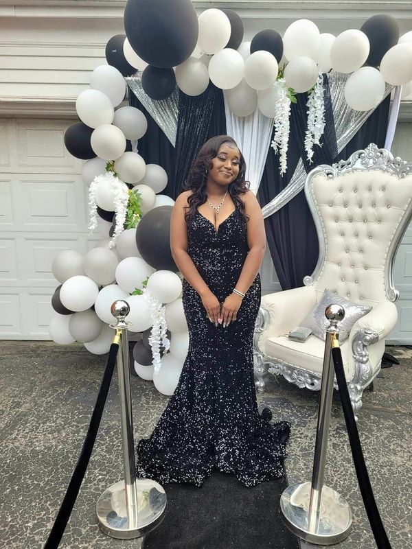 Woman in a sparkling black gown poses in front of black and white balloon decor.
