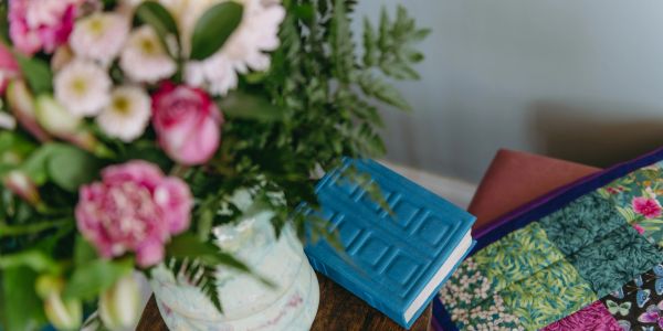 A bouquet of flowers, a blue book, and a colorful quilt on a wooden table.