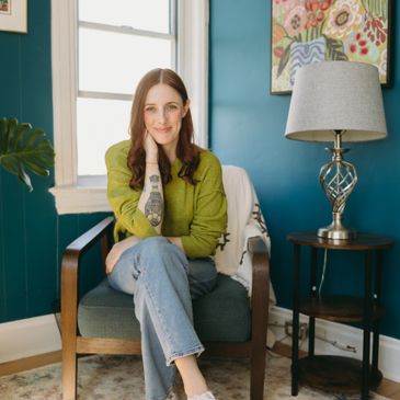 Young woman with tattoo sitting in a cozy chair in a colorful room.