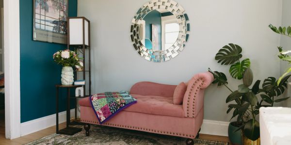 Cozy pink chaise lounge with a decorative mirror and plants in a stylish living room.