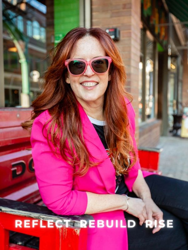 Smiling woman in pink jacket and sunglasses sitting on red bench outdoors.