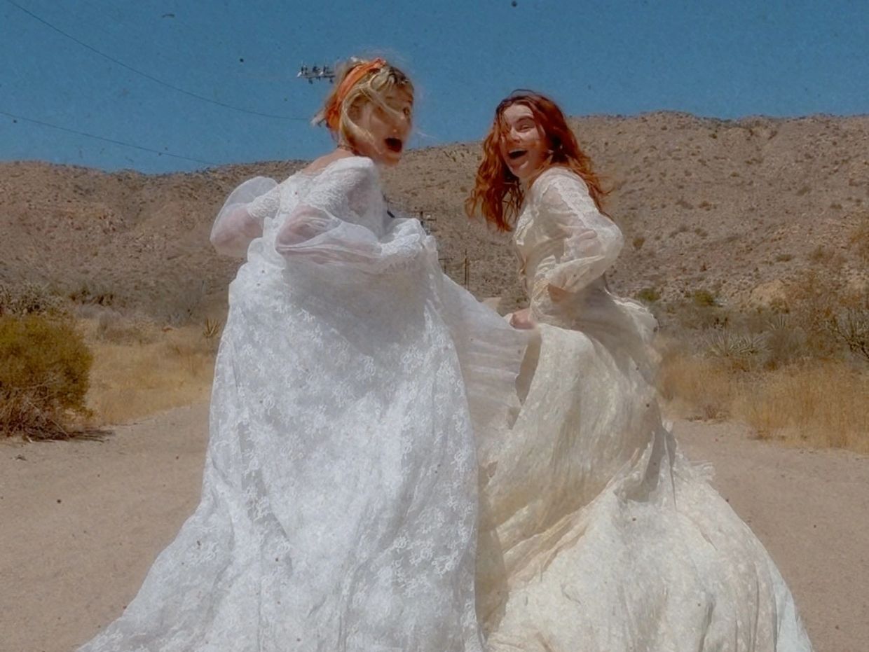 Two women running in long dresses somwhere in the sandy desert. 