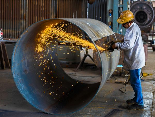 Worker grinding a large metal pipe, sparks flying.