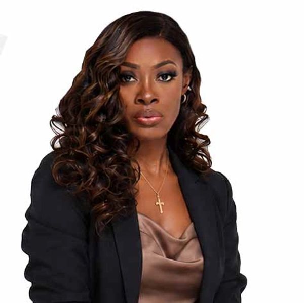 Confident woman with curly hair wearing a black blazer and cross necklace.