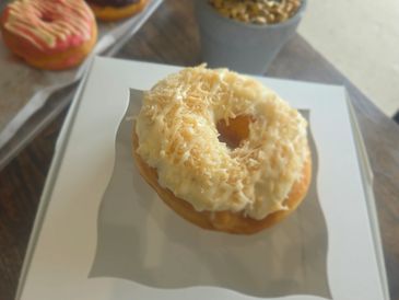 Toasted coconut donut with icing on a white plate.