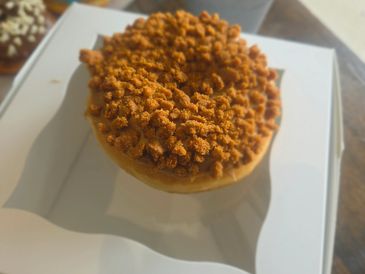 A donut with crumb topping in a white box.
