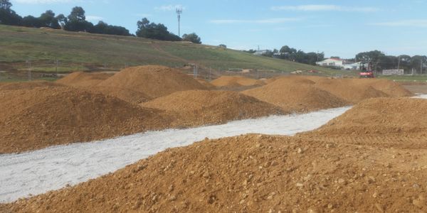 Several dirt mounds on a construction site with a gravel path.