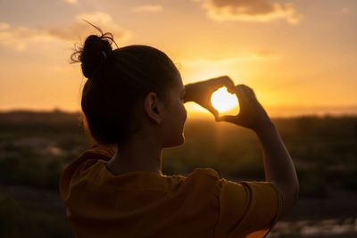 Person giving heart sign in sun