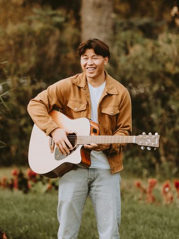 A young man playing guitar outdoors with a joyful expression.