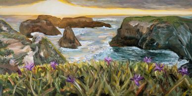 A coastal landscape with rocky cliffs and purple flowers at sunset.