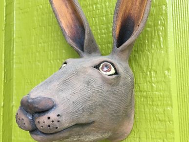 Close-up of a sculpted rabbit head mounted on a green wall.