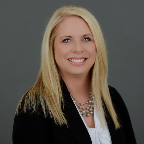 Professional woman with blonde hair smiling against a gray background.