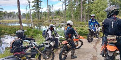 Group of motocross riders resting by a lake in the forest.