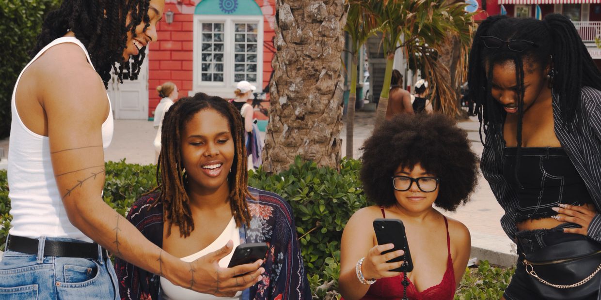 Four friends enjoying and sharing something on their smartphones outdoors.