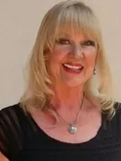 Smiling woman with blonde hair wearing black top and necklace.