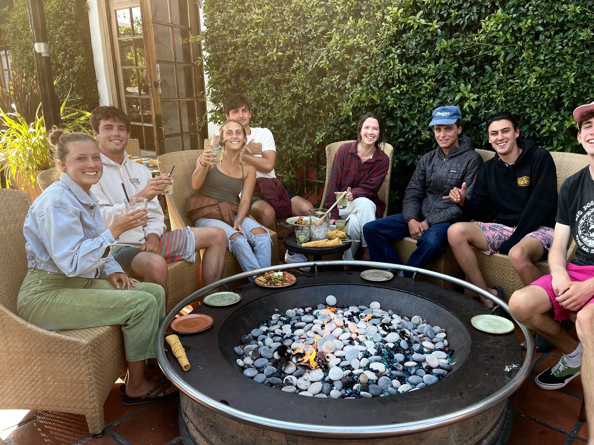 A group of friends enjoying drinks around an outdoor fire pit.
