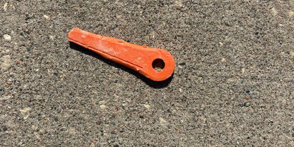 An orange plastic marker lies on rough asphalt ground.