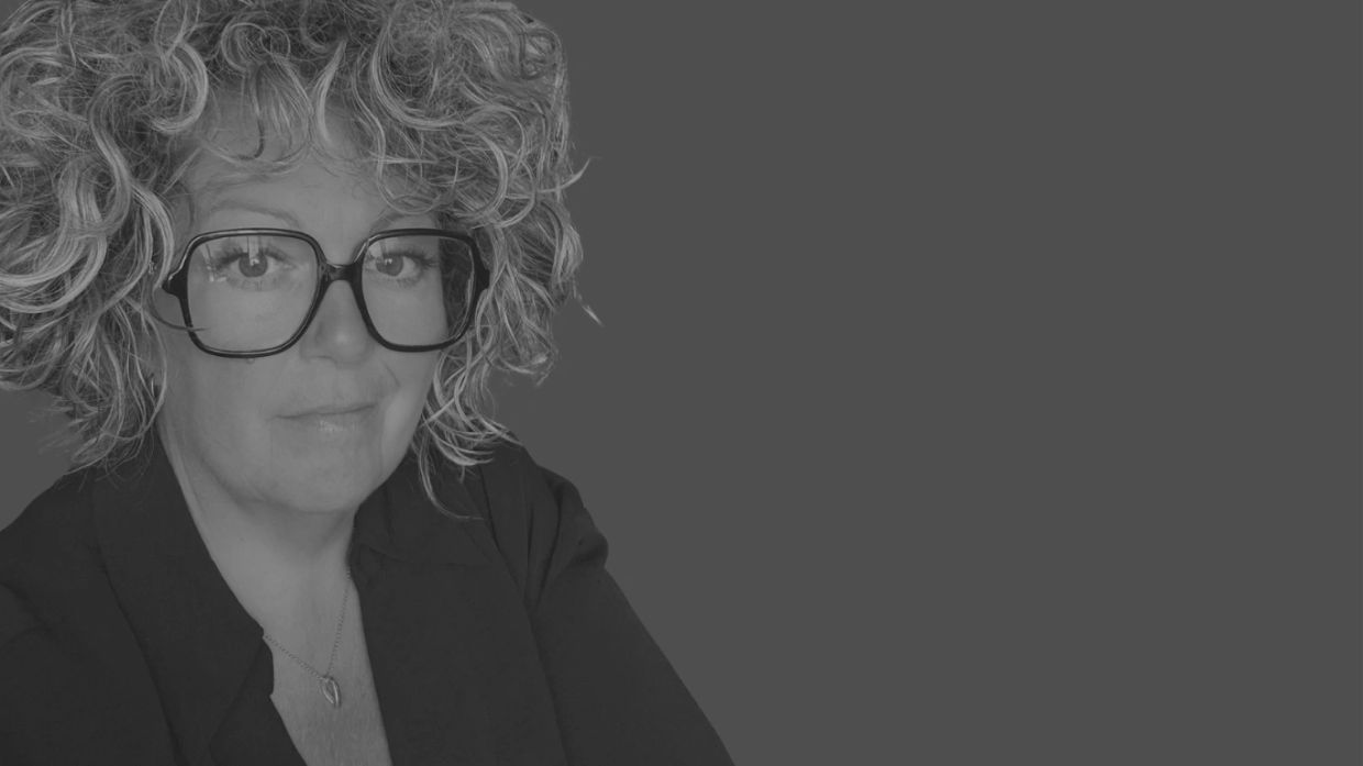 Femme aux cheveux bouclés et lunettes, regardant la caméra.
