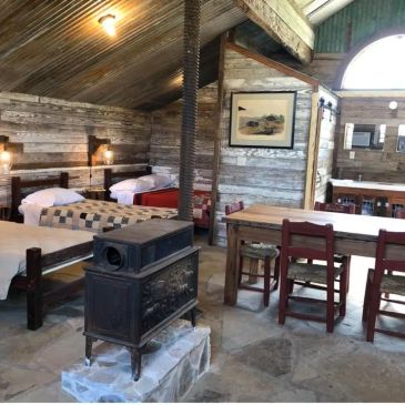 Rustic cabin interior with beds and wood stove.