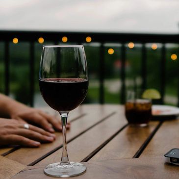 A glass of red wine on a wooden table with blurred background and hands.