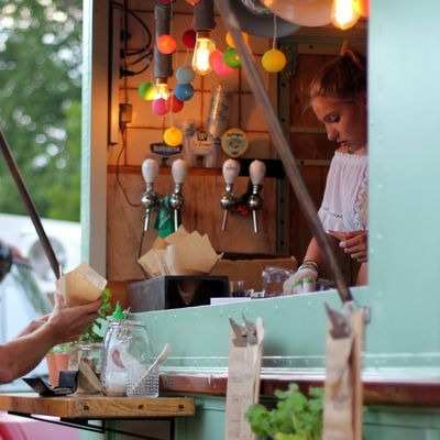 Woman serving at a colorful food truck with hanging lights.