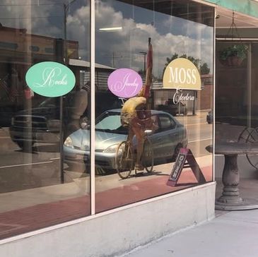 Reflection of a cyclist in a storefront window with colorful signs.