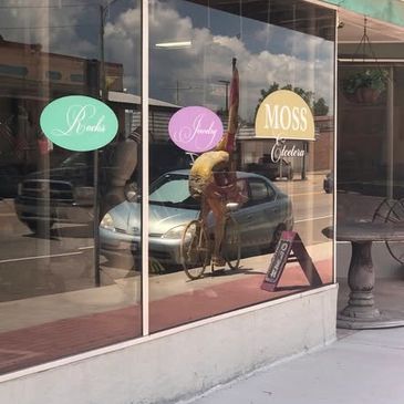 Reflection of a cyclist in a storefront window with colorful signs.