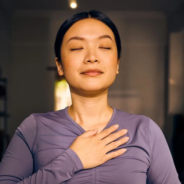 Woman with eyes closed and hand on chest, appearing calm and serene.