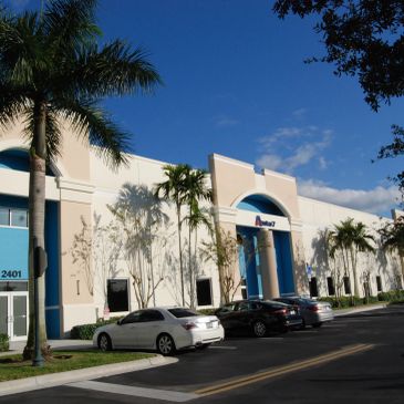 Modern office building with palm trees and cars parked outside.