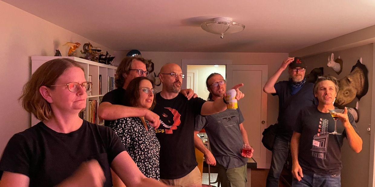 People in a room dancing, drinking and pointing at something not visible outside of the frame.