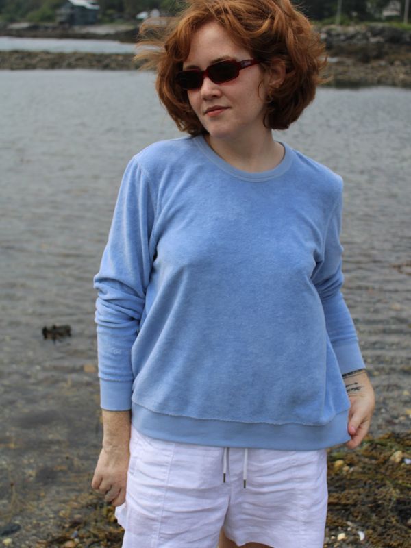 Woman in a blue sweater standing by the water.