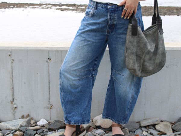 Person wearing blue wide-leg jeans and holding a gray bag.