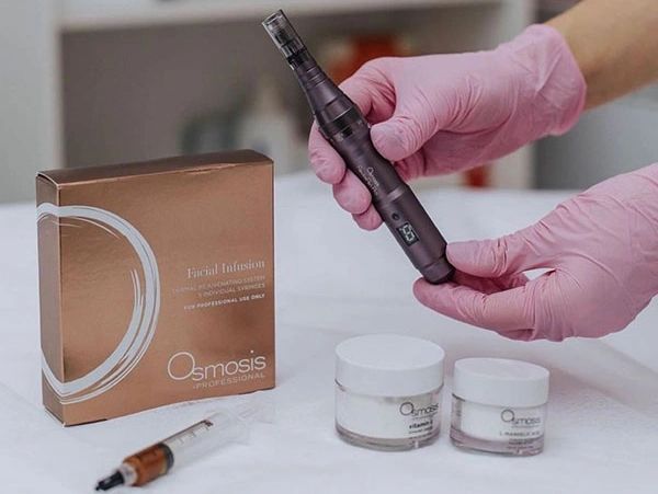 Hands wearing pink gloves hold a skincare device with Osmosis Professional products.