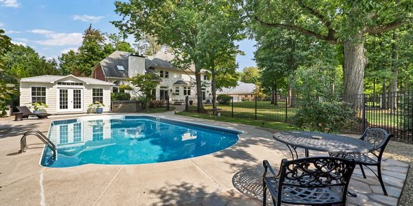 Backyard with a  swimming pool and patio furniture with trees. Pool house and home in background.