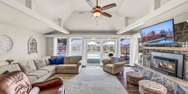 Spacious neutral living room with ample seating, fireplace, & large flatscreen. Pool in background.