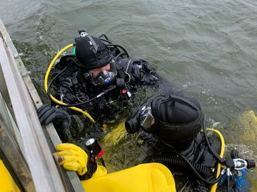 Public Safety divers in the water holding on to the side of a boat