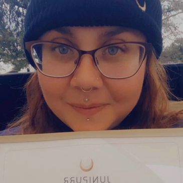 Person wearing a beanie and glasses holding a JuniPurr certificate.
