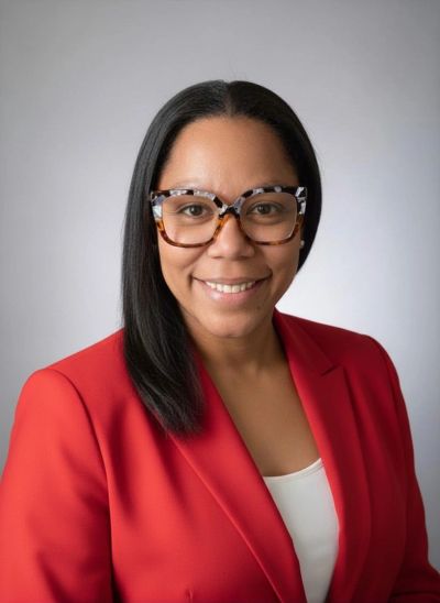 Professional woman smiling, wearing tortoiseshell glasses and a red blazer.