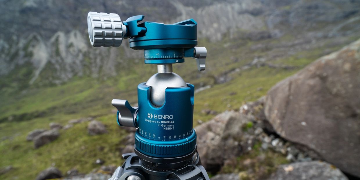 Close-up of a blue Benro tripod ball head in a mountainous outdoor setting.
