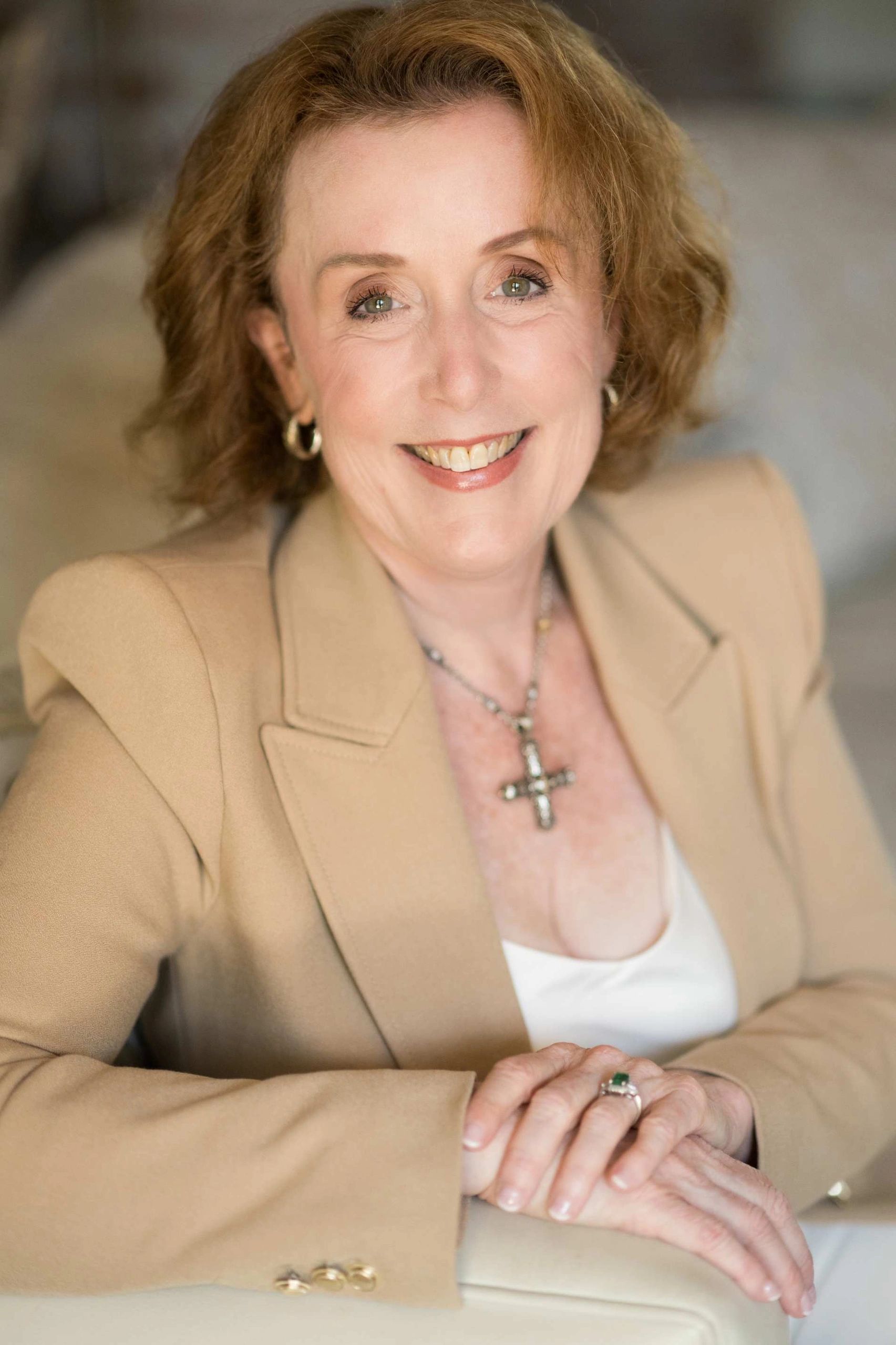 JoAnn Andrews smiling confidently in a beige blazer, seated indoors, representing clarity and leader