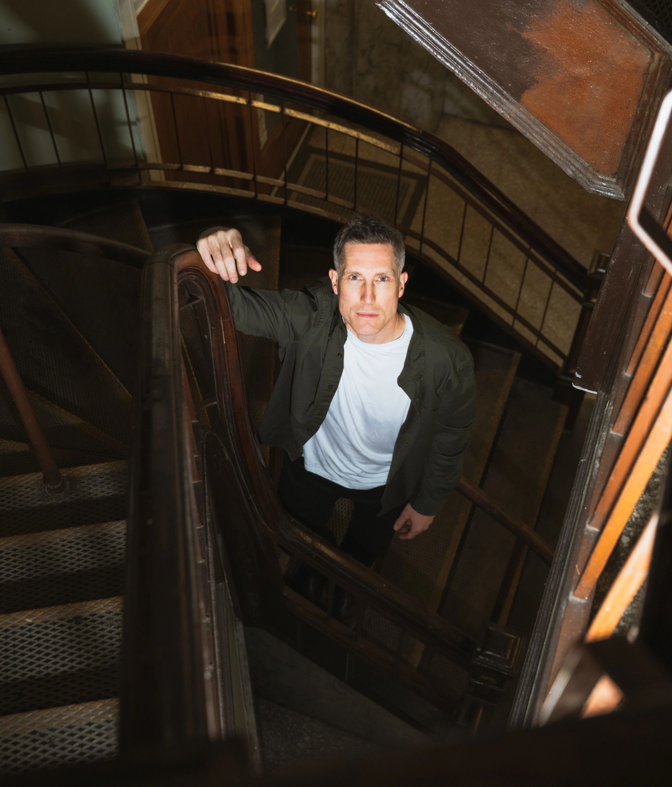 Bio for RJW Leadership. Image of Ryland Wellwood, standing in a stairwell looking up at the viewer.