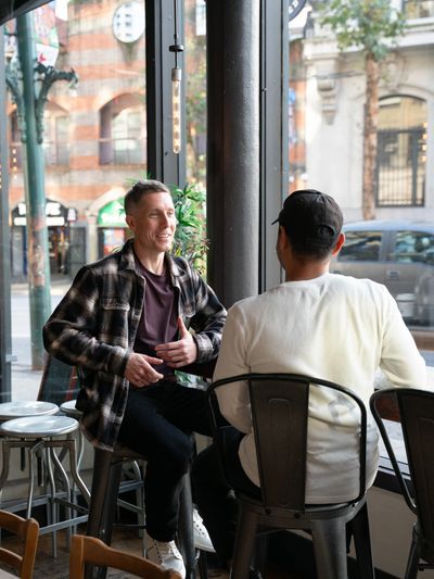 Ryland Wellwood coaching a person while they sit together in a cafe.