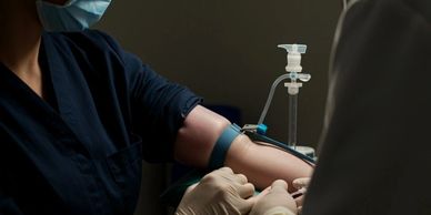 Healthcare worker drawing blood from a patient's arm wearing masks.