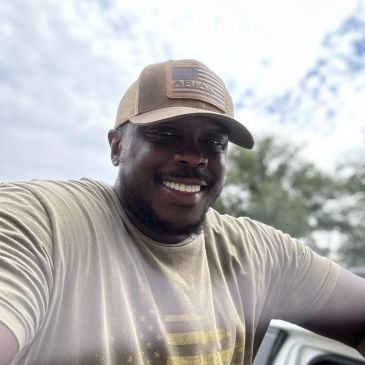 Man smiling outdoors in a cap and t-shirt.